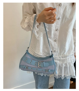 Light blue Y2K denim saddle bag with silver studs and leather trim on a white lace top