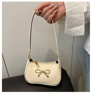 Détail du sac sous le bras blanc cassé avec texture litchi et nœud doré élégant