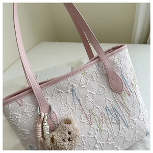 Detail of white embossed tote bag with pink handles and a cute plush bear charm