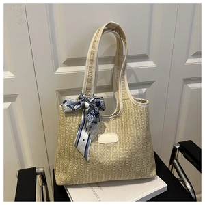 Detail of a straw tote bag with woven texture, leather handles, and a floral scarf