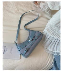Detail of light blue crescent underarm bag with silver buckles on white bedding