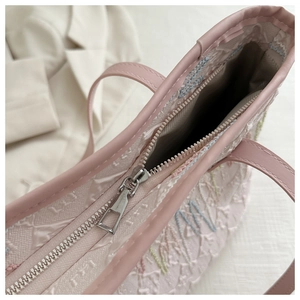Detail shot of the pink tote bag featuring embroidery, silver zipper, and textured fabric