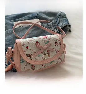 Détail d'un sac bandoulière rose avec motifs cartoon, nœud 3D et pendentif cœur en métal