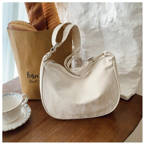 Detailed view of the creamy white crescent bag featuring pleated texture and adjustable strap