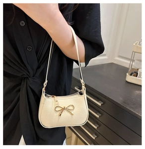 Détail du sac sous l'aisselle crème avec nœud doré et texture cuir grainé