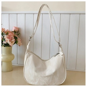 Detail of white dumpling bag showing pleated texture and silver zipper on wooden background