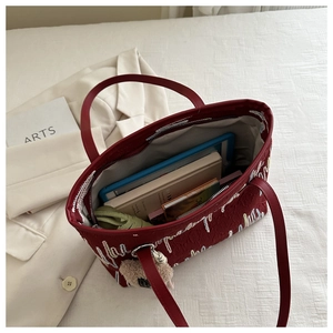 Top view of red embroidered tote bag filled with everyday items like tablets and notebooks