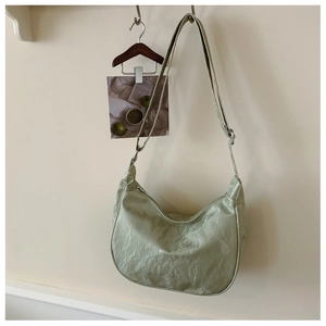 Detail of mint green pleated crescent bag with adjustable strap on a minimalist wall