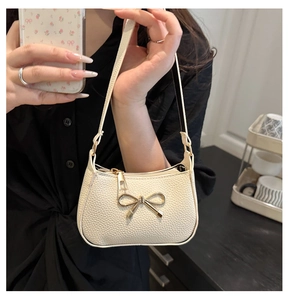 Détail du sac sous le bras en similicuir blanc crème avec nœud papillon doré chic