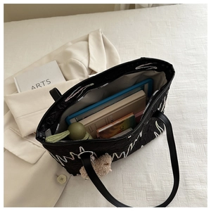 Detail of spacious black tote bag featuring colorful wave embroidery and a cute bear charm
