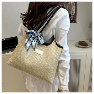 Close-up of woven straw tote bag with black leather trim and floral silk scarf detail