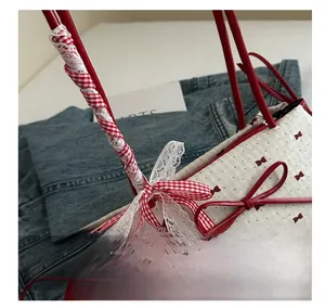 Close-up of cream underarm bag with red bow print and lace-wrapped handles on denim