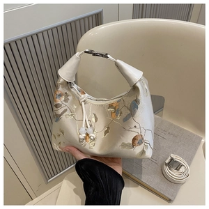 Detail of cream brocade handbag featuring floral embroidery and leather handle with metal clasp