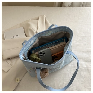 Top view of blue textured tote bag interior with embroidery and plush bear charm