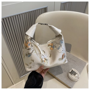 Detail view of cream dumpling bag with bird embroidery and silver hardware accents