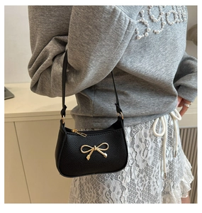 Close-up of black textured leather shoulder bag featuring a gold bow metallic buckle
