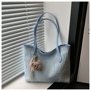 Detail of light blue quilted tote bag with a small brown plush bear charm and thin straps