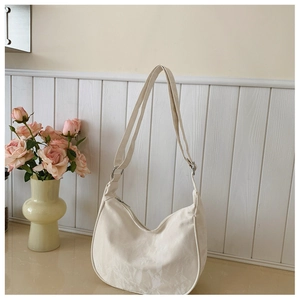 Detail of cream-white crescent dumpling bag showing canvas texture and adjustable strap