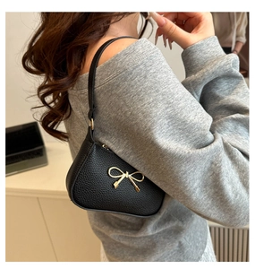 Détail du sac baguette en cuir noir avec boucle nœud doré porté à l'épaule par un mannequin