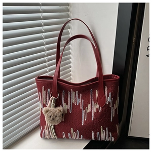 Detail of red tote bag with colorful wave embroidery and brown plush bear charm