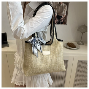 Detail of woven straw tote bag with black leather trim and vintage Paris print scarf