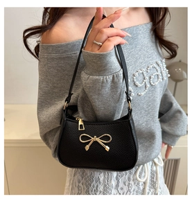 Détail d'un sac sous le bras en cuir grainé noir avec un nœud doré métallisé