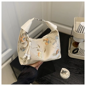 Close-up of cream satin handbag featuring delicate bird and flower embroidery and metal buckle