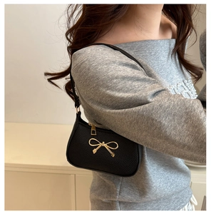 Détail du sac sous l'aisselle en cuir noir avec boucle nœud doré porté par modèle