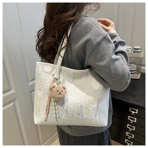 Detail of white textured tote bag with colorful wavy embroidery and plush bear charm