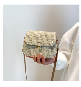 Detailed view of beige straw saddle bag featuring white floral embroidery and gold lock