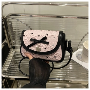Détail du sac bandoulière rose plissé avec nœuds noirs et pendentif en forme de cœur