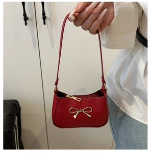 Détail d'un sac à main rouge en similicuir avec un nœud doré et une fermeture éclair