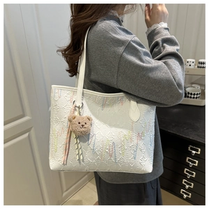 Detailed look at white quilted tote bag with color embroidery and plush bear charm