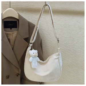 Detail view of cream dumpling bag featuring textured pattern and white plush bear charm