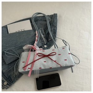 Détail du sac bandoulière bleu clair à carreaux avec nœuds rouges et breloque dentelle