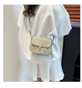 Detail of woven straw saddle bag featuring delicate white floral embroidery and gold clasp