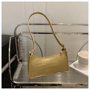 Close-up of golden faux leather baguette bag with crocodile texture on a coffee table