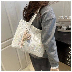 Close-up of white tote bag with embossed pattern and cute brown plush bear accessory