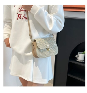 Detail of woven straw shoulder bag featuring white floral embroidery and gold buckle