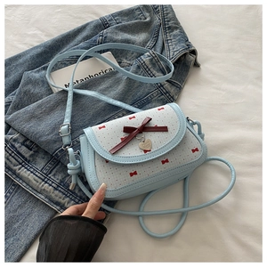 Détail du sac bandoulière bleu clair avec imprimé nœud rouge et pendentif cœur argenté