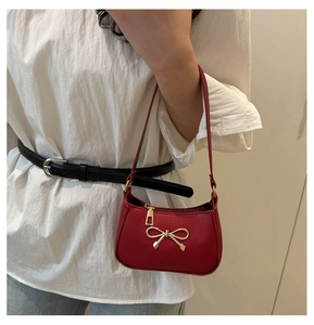 Détail du sac sous l'aisselle en cuir rouge avec nœud doré et fermeture éclair