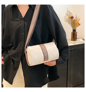Detail of cream leather cylinder bag with textured wide woven shoulder strap on model