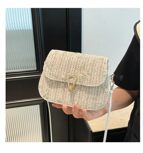 Detail of beige straw saddle bag featuring green floral embroidery and gold U-shaped buckle