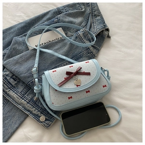 Détail du sac bandoulière bleu clair avec nœuds rouges et breloque en forme de cœur