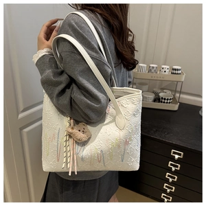 Detail of white tote bag with colorful wave embroidery and brown plush bear charm