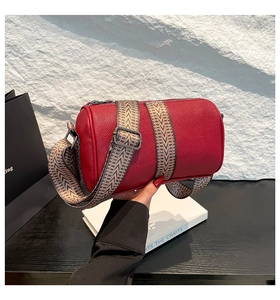 Detailed view of a red leather cylindrical crossbody bag with woven shoulder strap