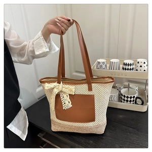 Detail of hand-woven straw tote bag featuring brown leather trim and a lace ribbon bow