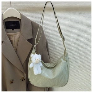 Close-up of sage green dumpling bag with pleated texture and a cute plush bear pendant