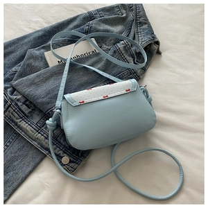 Vue à plat d'un sac bandoulière bleu ciel avec motifs papillons sur une veste en jean