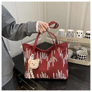 Close-up of red tote bag featuring colorful vertical embroidery and a plush bear charm